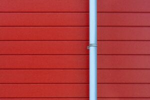 A minimalist photo of a red wall with a white rain gutter, showing clean lines and vibrant color contrast.